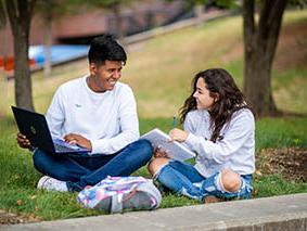 Two people sitting on the grass talking to each other